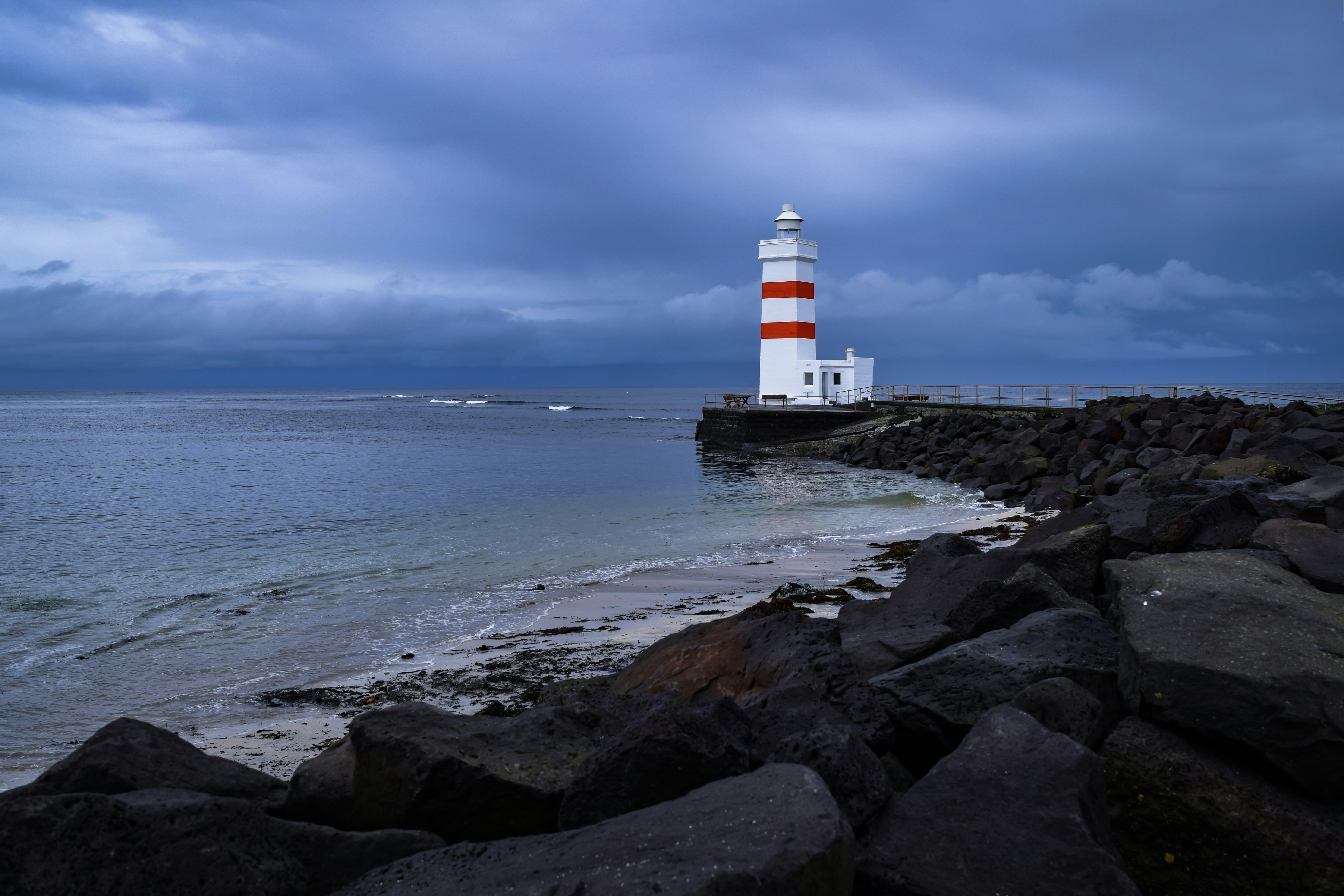 white and red lighthouse on brown rocky shore during daytime